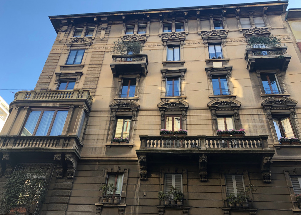 Häuserfassade vor strahlend blauem Himmel, von untern aufgenommen. Die Fenster mit Halbsäulen und halbrunden Giebeln. Vereinzelt sind Balkone angebracht und an der linken Bildseite ist ein verzierter schmaler Erker zu sehen. 