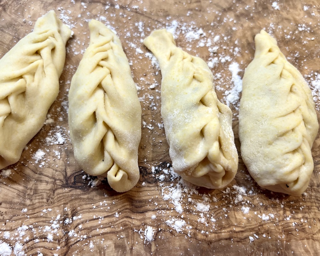 Auf einem Holzbrett liegen nebeneinander die sardischen Ravioli Culurgiones. Deutlich zu sehen ist die Sa Spighitta - der an eine Ähre erinnernde Verschluss. Culurgiones sind gefüllt mit einer Kartoffel-Minz-Pecorino-Füllung