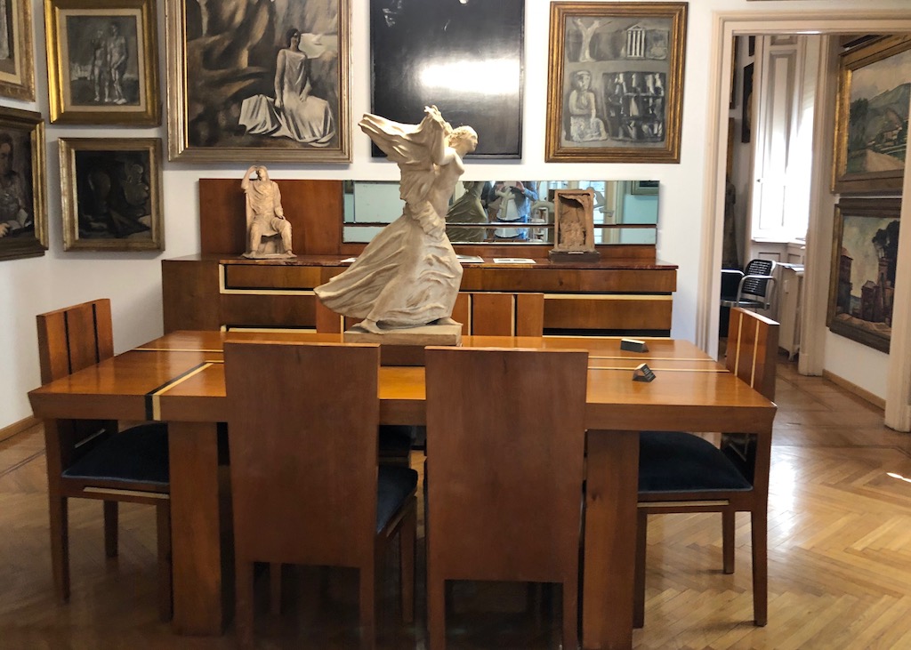 Casa museo Boschi di Stefano Case museo - museale Häuser in Mailand. Blicj ins Esszimmer des Casa Museo Boschi di Stefano. Gemaälde übereinander angeordnete Gemälde zieren die Wände. Auf dem eckigen Holztisch, ringsum mit Holzstühlen, steht eine weiße Marmorskulptur