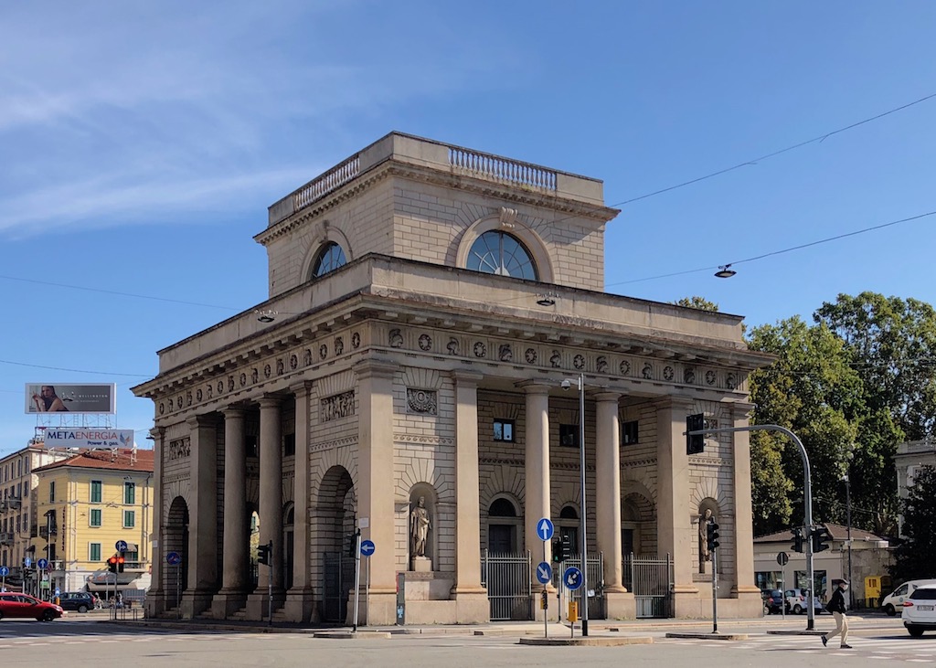 Ein quaderförmiges, helles Gebäude mit einem kleinen quadratischen Türmchen obendrauf - die Porta Venezia in Mailand. 