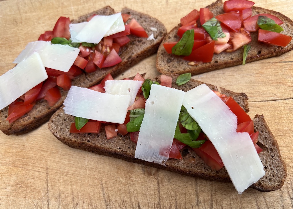 Bruschetta, Crostini, Tramezzini, Tartine - Was ist der Unterschied? Bildfüllend liegen drei Scheiben geröstetes Brot (Bruschette), die mit Tomatenstückchen, Basilikumblättchen belegt sind. Zwei Scheiben sind zusätzlich noch mit schmalen Pecorinoscheiben belegt.