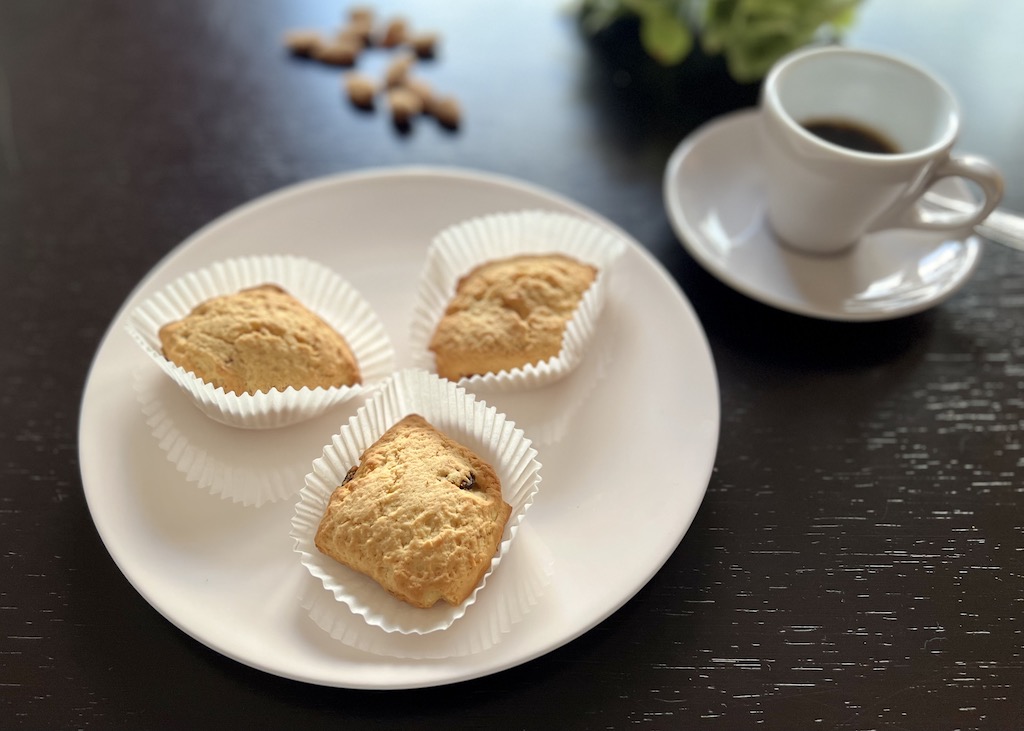 Papassinos oder Pappassini Auf einem rosafarbenen Teller liegen drei Papassinos. Daneben steht eine Espressotasse mit Cafè darin. Im Hintergrund liegen ein paar Mandeln.